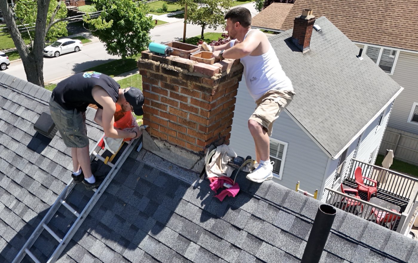 The founder at work on a rooftop, rebuilding a brick chimney with a crew member